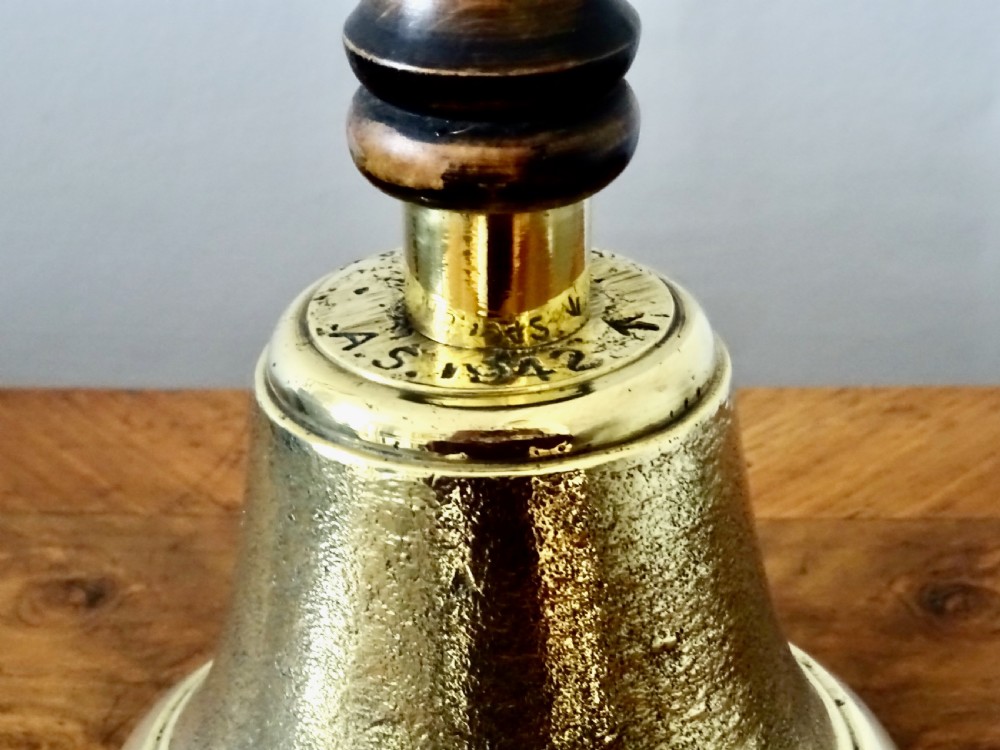 A cast brass hand bell featuring a turned dark wood handle and stamped military markings dated 1942. View VI