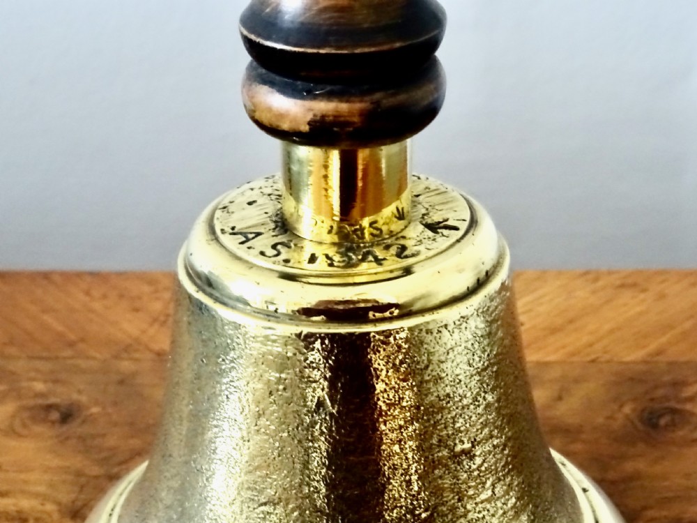 A cast brass hand bell featuring a turned dark wood handle and stamped military markings dated 1942. View X