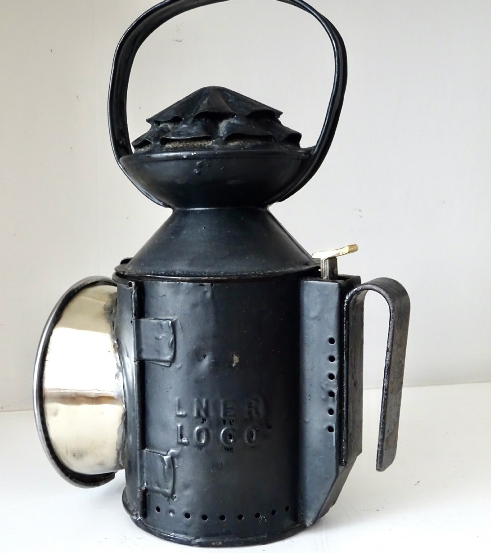 A black painted metal railway oil lantern featuring a hinged glass lens door, carrying handle, and internal brass oil burner. View III