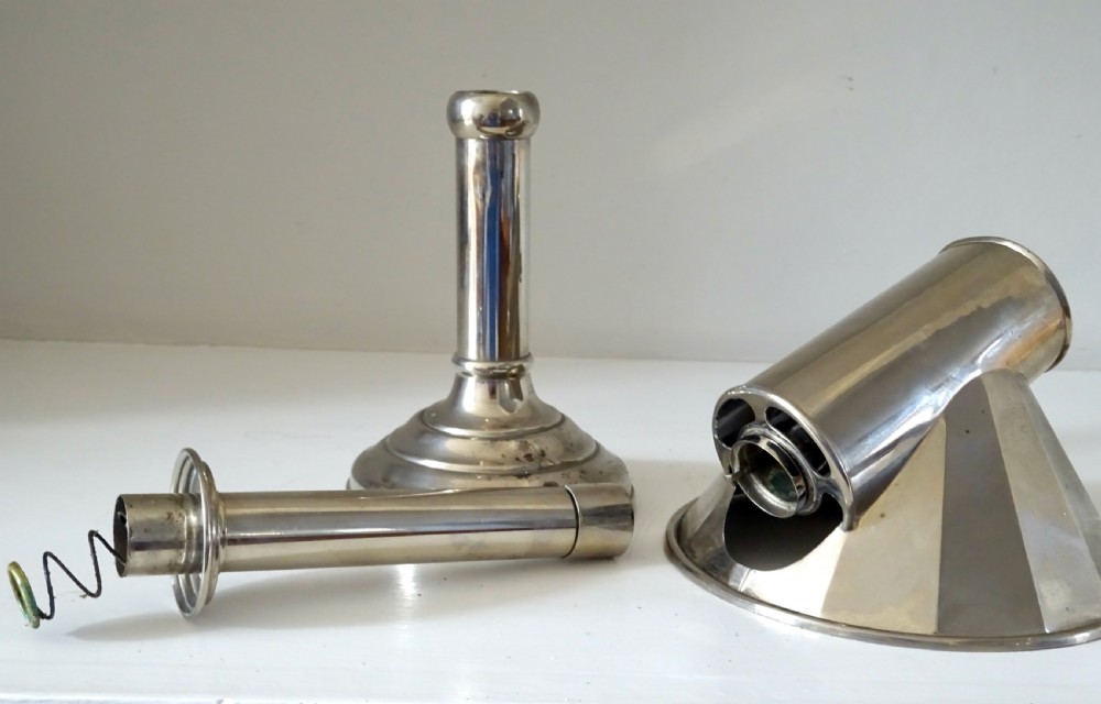 A nickel-plated antique candle lamp featuring a stepped circular base, tubular stem, and a curved fan-like reflector hood attached near the candle nozzle. View IV