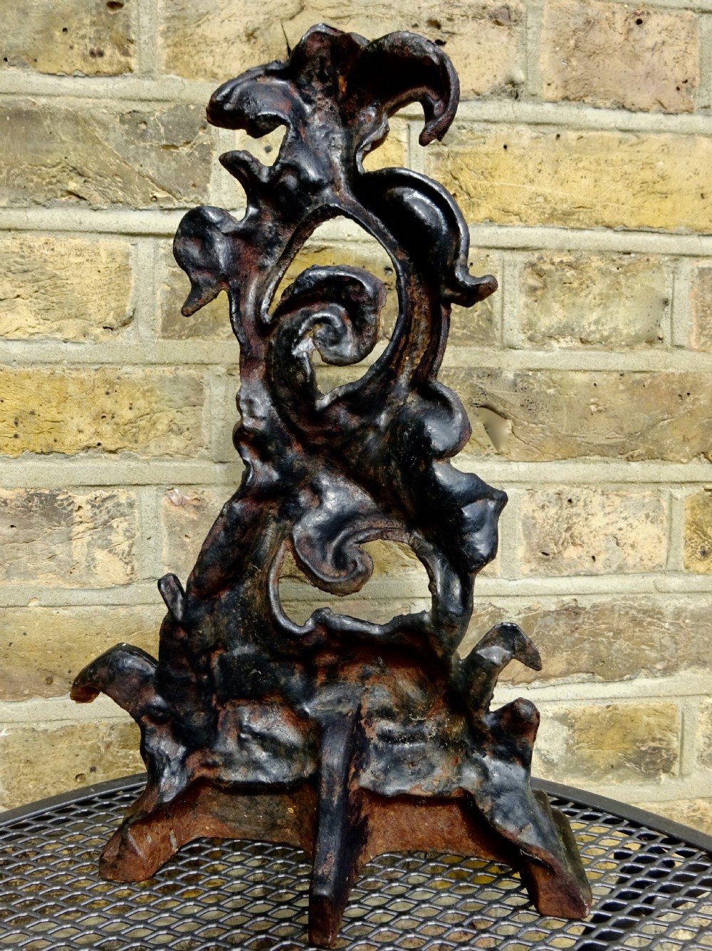 A heavy black cast iron doorstop featuring a mythological dolphin intertwined with acanthus scrollwork set upon a rectangular molded base. View VI