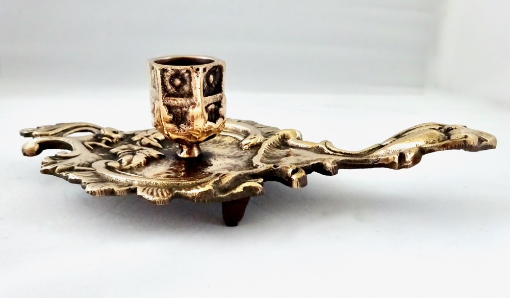 An antique cast bronze chamberstick featuring an extended handle, foliate relief tray, and a hexagonal candle socket. View VI