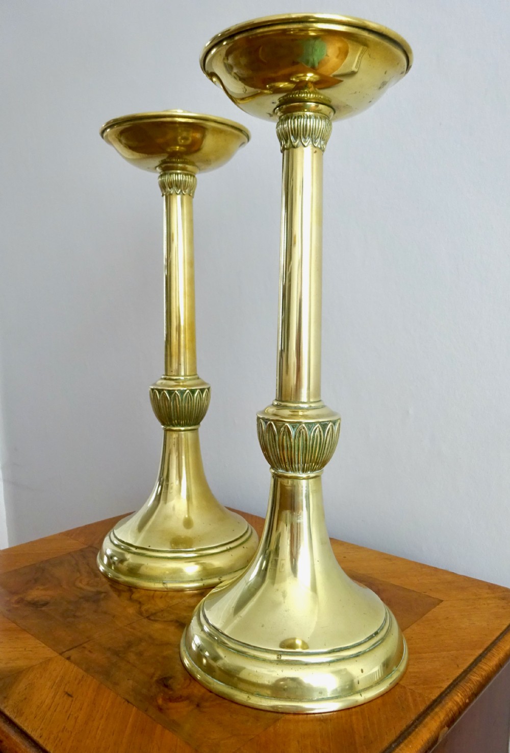 A pair of tall, polished brass candlesticks featuring turned shafts, carved leaf motif knops, circular bases, and wide upper sconces.