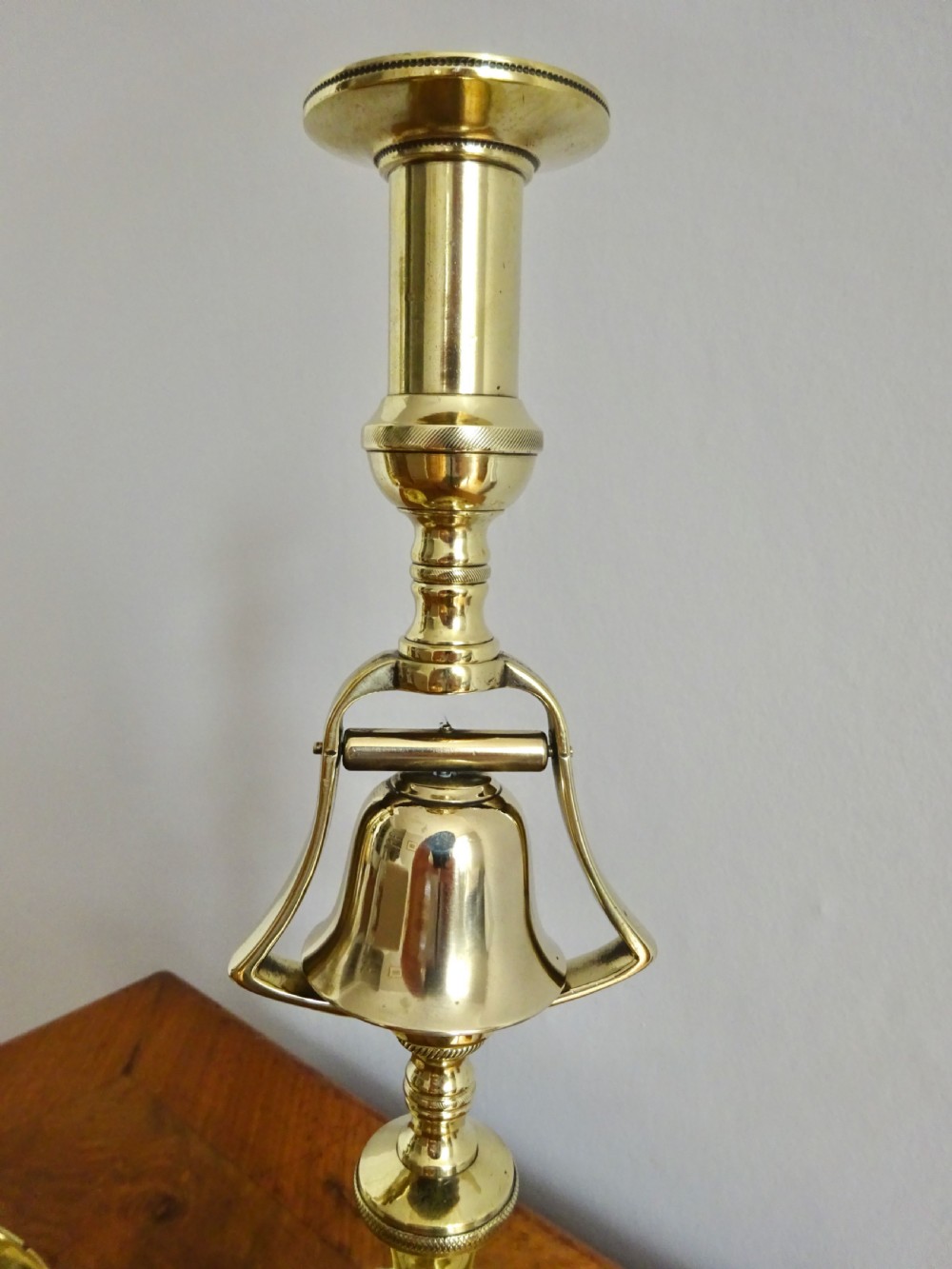 A pair of polished brass Victorian tavern candlesticks featuring turned stems, hanging bells suspended in frames, and wide saucer bases. View II