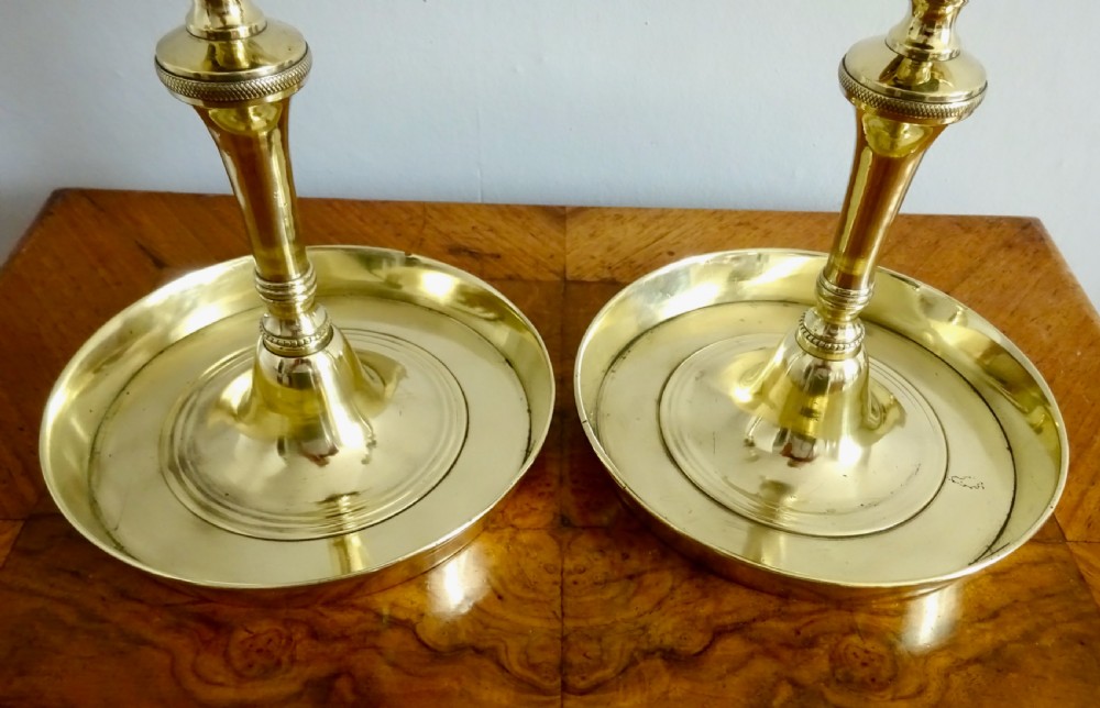 A pair of polished brass Victorian tavern candlesticks featuring turned stems, hanging bells suspended in frames, and wide saucer bases. View IV