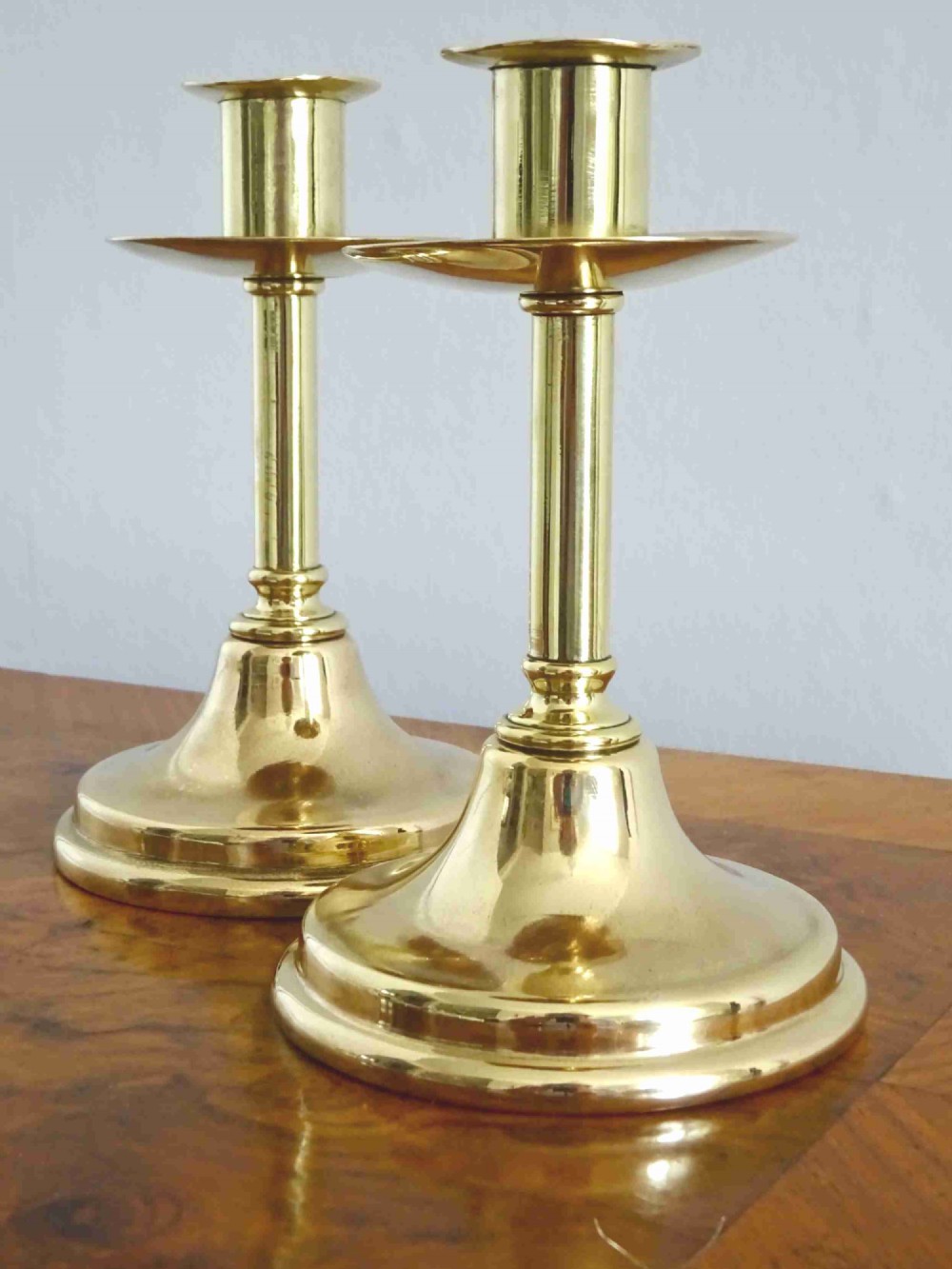 A pair of polished late Victorian brass candlesticks featuring turned column stems, wide drip pans, and flared circular bases.