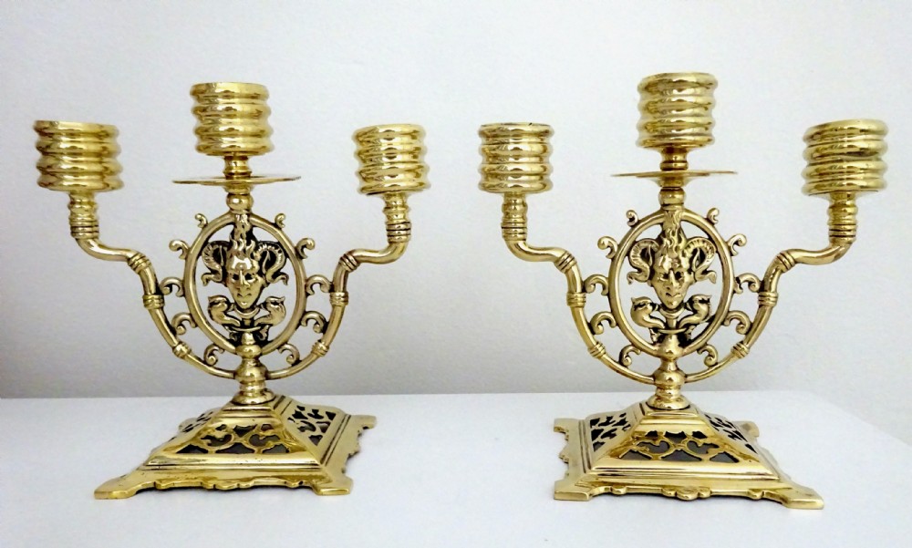 A pair of cast brass three-light candelabras featuring central grotesque mask motifs and pierced square bases.