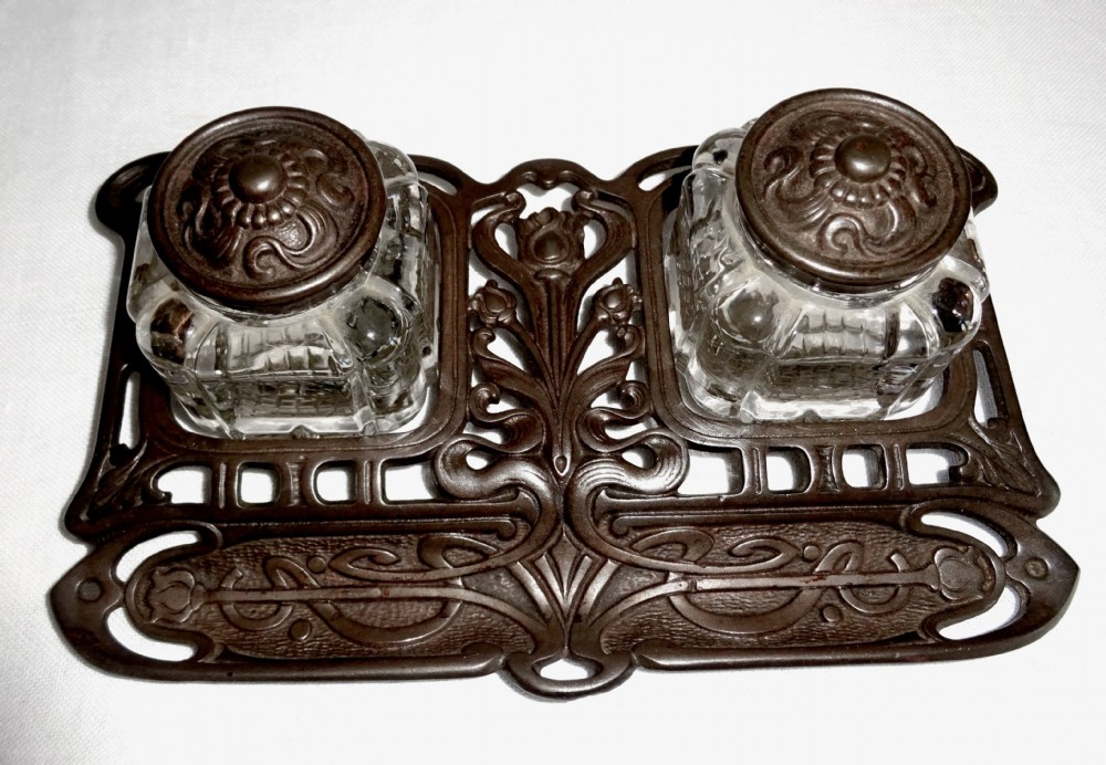 An Art Nouveau dark metal double inkstand featuring pierced floral scrollwork and two square glass inkwells with embossed metal lids. View VII