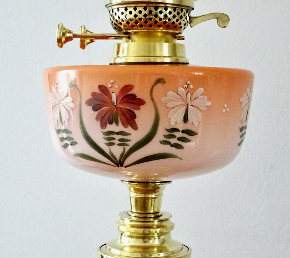 An antique oil lamp featuring a brass pedestal base, a hand-painted floral glass font, and a flared ruffled glass shade. View II