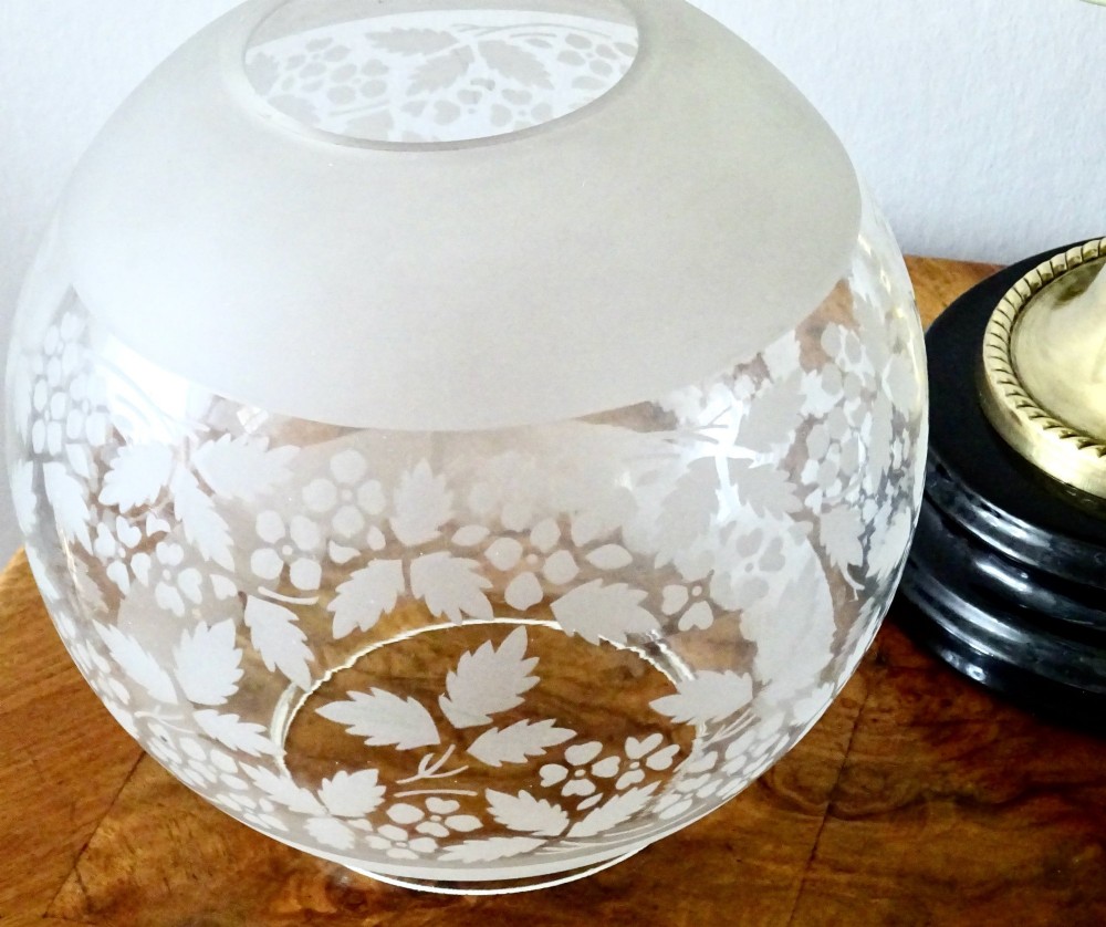 An antique brass oil lamp featuring a hand-painted floral glass font, a frosted etched globe shade, and a tall clear glass chimney on a stepped circular base. View V