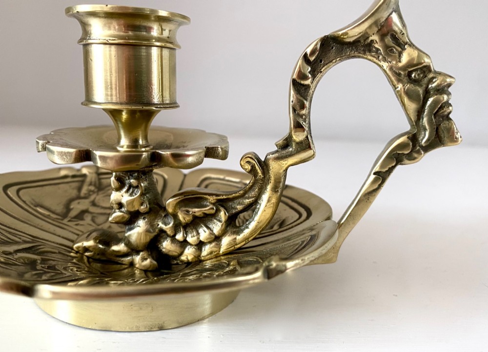An antique French brass chamberstick featuring a scalloped tray base, turned candle socket, and a cast handle shaped like a grotesque face. View V