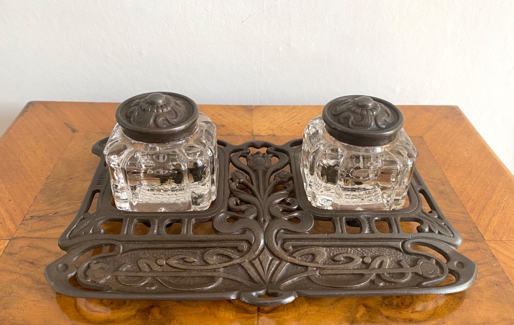 An Art Nouveau dark metal double inkstand featuring pierced floral scrollwork and two square glass inkwells with embossed metal lids. View II