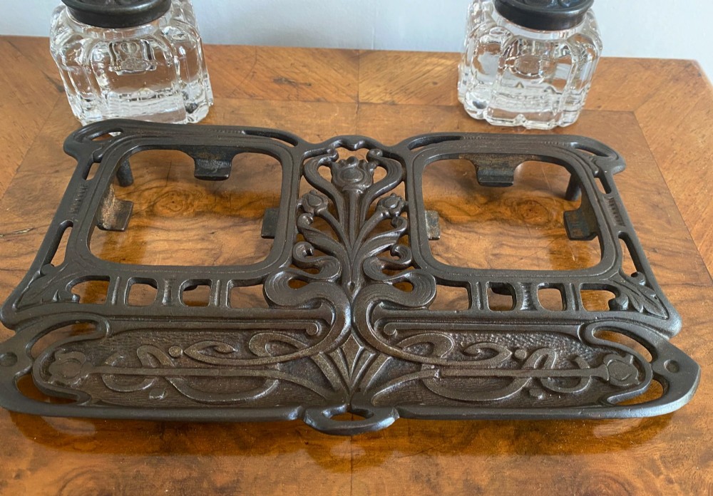 An Art Nouveau dark metal double inkstand featuring pierced floral scrollwork and two square glass inkwells with embossed metal lids. View IV
