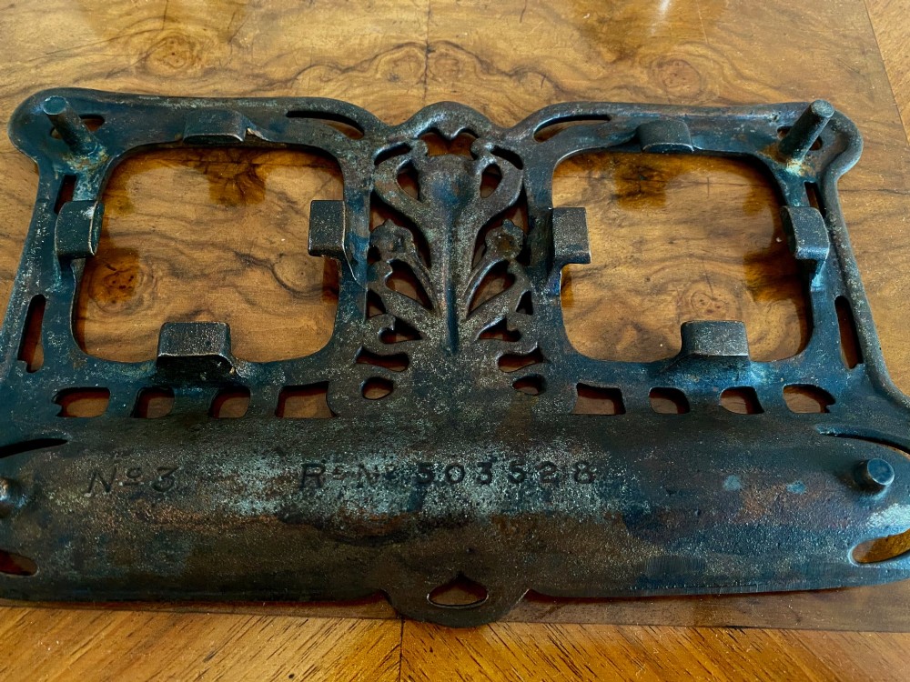 An Art Nouveau dark metal double inkstand featuring pierced floral scrollwork and two square glass inkwells with embossed metal lids. View V