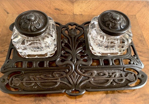 An Art Nouveau dark metal double inkstand featuring pierced floral scrollwork and two square glass inkwells with embossed metal lids. View VII