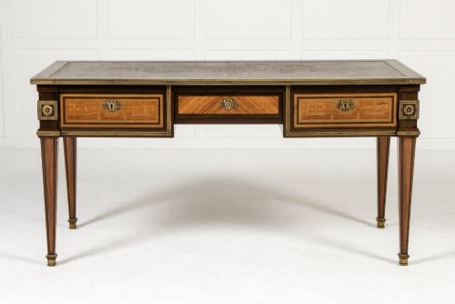 fig 1. A 19th-century French Louis XVI style bureau plat writing desk featuring geometric parquetry inlay, three frieze drawers, a leather top insert, and brass mounts on square tapered legs.