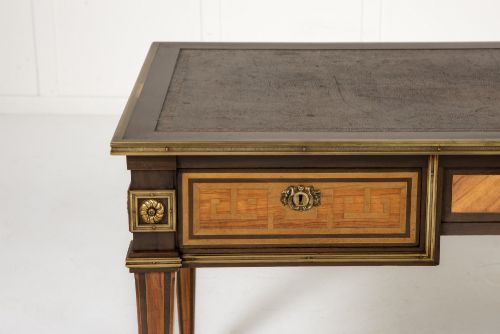 fig 2. A 19th-century French Louis XVI style bureau plat writing desk featuring geometric parquetry inlay, three frieze drawers, a leather top insert, and brass mounts on square tapered legs.