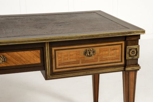 fig 3. A 19th-century French Louis XVI style bureau plat writing desk featuring geometric parquetry inlay, three frieze drawers, a leather top insert, and brass mounts on square tapered legs.