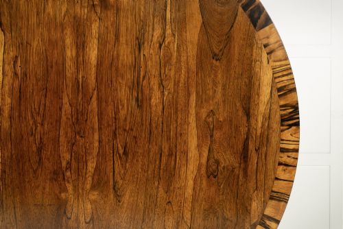 fig 1. A 19th-century English Regency circular rosewood centre table displayed with its crossbanded tilt-top tilted upright on a carved pedestal base with brass castors.
