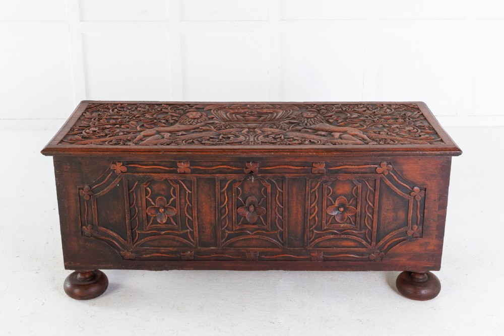 A 19th-century dark hardwood trunk featuring relief carvings of lions on the lid, carved floral front panels, and turned bun feet.