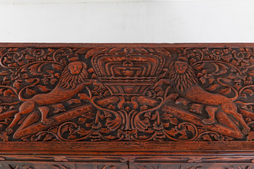 A 19th-century dark hardwood trunk featuring relief carvings of lions on the lid, carved floral front panels, and turned bun feet. View III