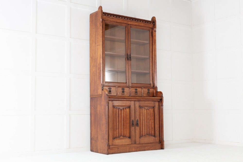 A tall nineteenth-century solid oak glazed bookcase featuring upper glass doors, four central drawers, and lower cupboard doors with carved linenfold panels. View II