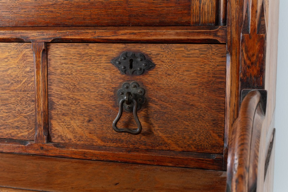 A tall nineteenth-century solid oak glazed bookcase featuring upper glass doors, four central drawers, and lower cupboard doors with carved linenfold panels. View III