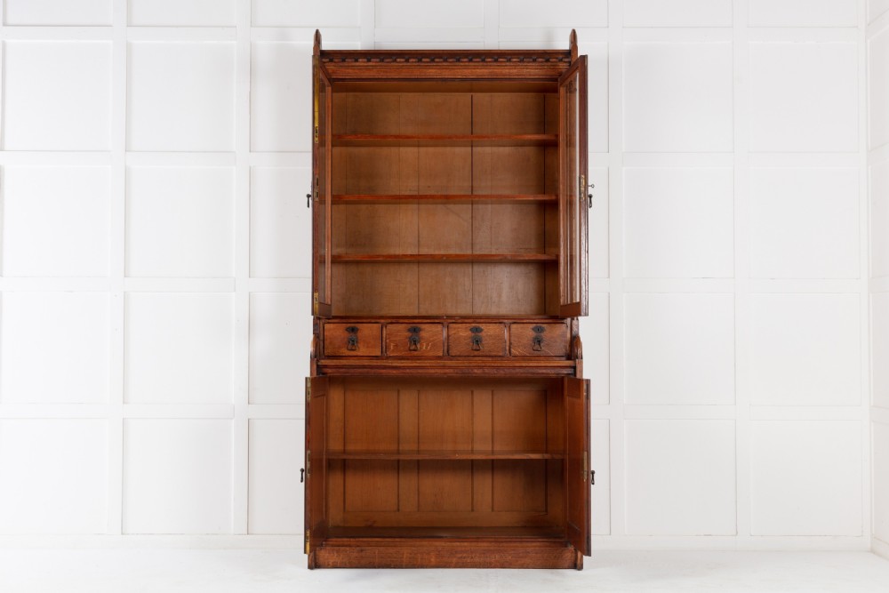 A tall nineteenth-century solid oak glazed bookcase featuring upper glass doors, four central drawers, and lower cupboard doors with carved linenfold panels. View IV