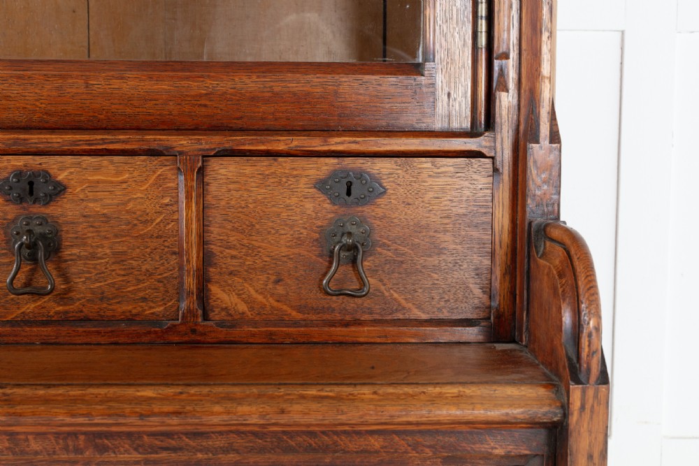 A tall nineteenth-century solid oak glazed bookcase featuring upper glass doors, four central drawers, and lower cupboard doors with carved linenfold panels. View V