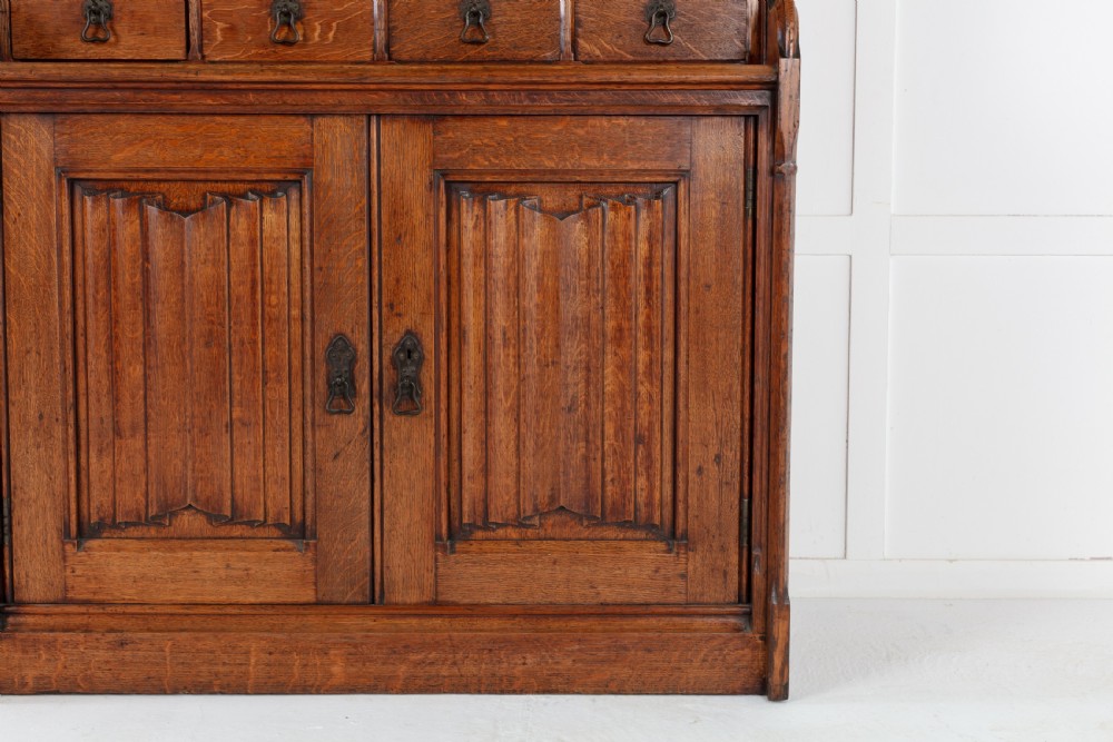 A tall nineteenth-century solid oak glazed bookcase featuring upper glass doors, four central drawers, and lower cupboard doors with carved linenfold panels. View VI