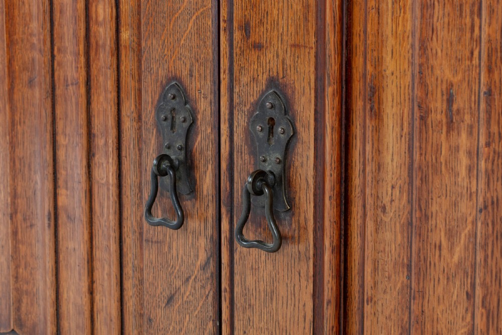 A tall nineteenth-century solid oak glazed bookcase featuring upper glass doors, four central drawers, and lower cupboard doors with carved linenfold panels. View VII