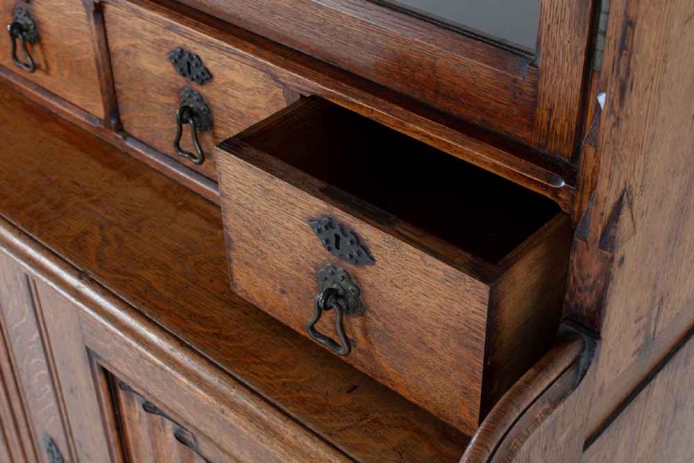 A tall nineteenth-century solid oak glazed bookcase featuring upper glass doors, four central drawers, and lower cupboard doors with carved linenfold panels. View IX