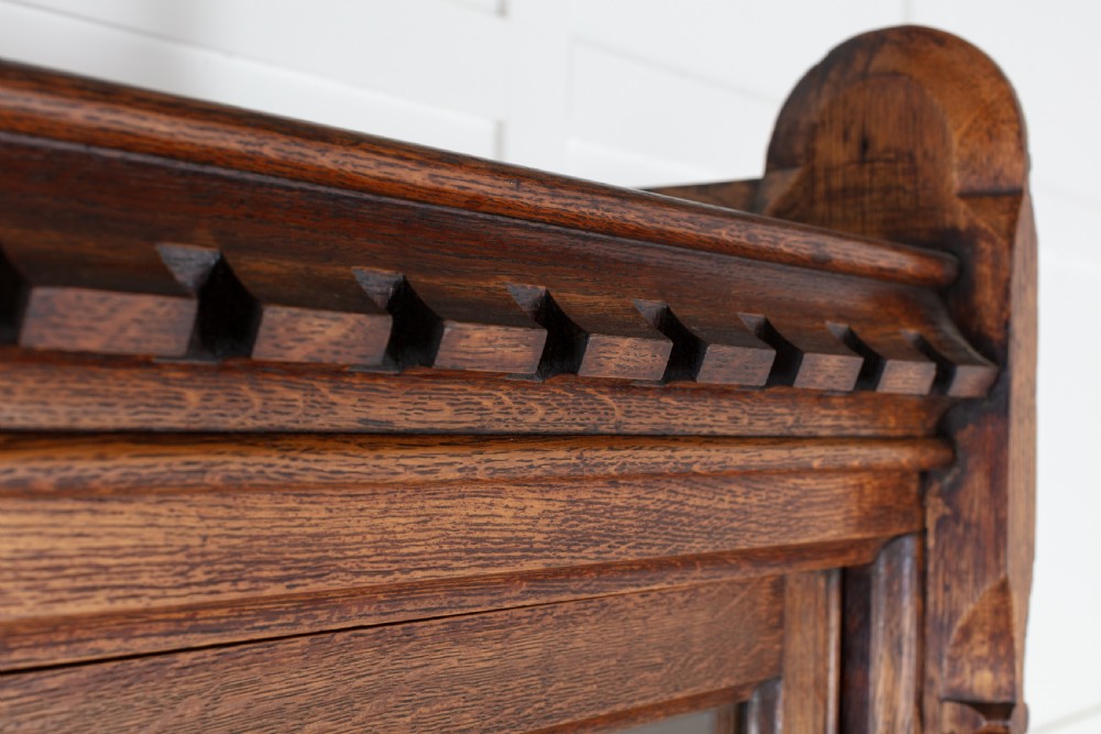 A tall nineteenth-century solid oak glazed bookcase featuring upper glass doors, four central drawers, and lower cupboard doors with carved linenfold panels. View XI