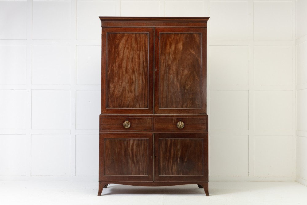 A George III mahogany linen press featuring flame mahogany panelled doors, brass handles, and splayed bracket feet.