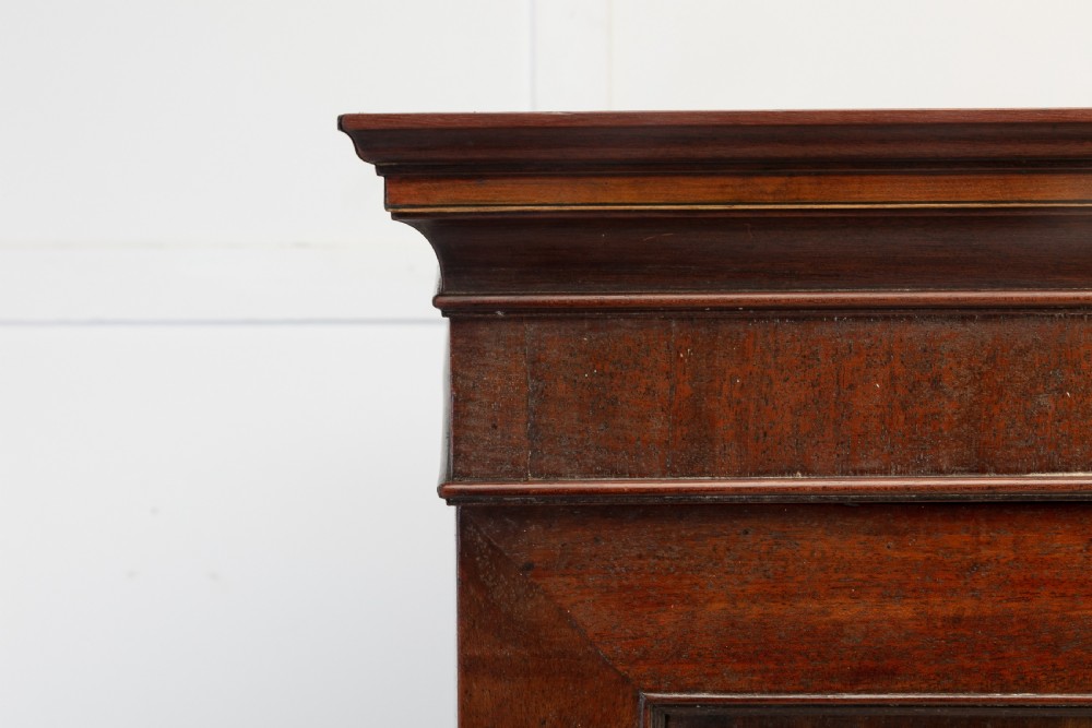 A George III mahogany linen press featuring flame mahogany panelled doors, brass handles, and splayed bracket feet. View IV