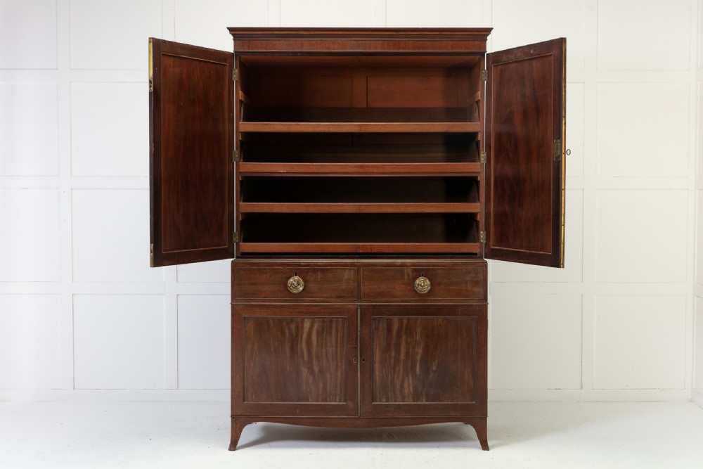 A George III mahogany linen press featuring flame mahogany panelled doors, brass handles, and splayed bracket feet. View V