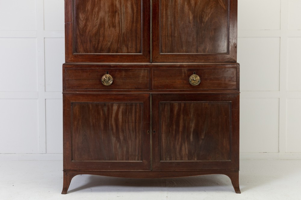 A George III mahogany linen press featuring flame mahogany panelled doors, brass handles, and splayed bracket feet. View VI