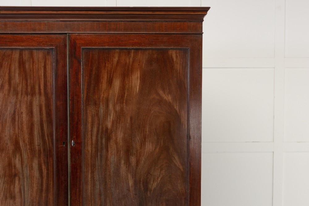 A George III mahogany linen press featuring flame mahogany panelled doors, brass handles, and splayed bracket feet. View VIII
