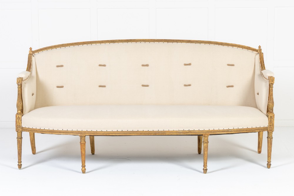 A 19th-century French sofa featuring a carved giltwood frame with fluted legs, curved backrest, and off-white fabric upholstery.