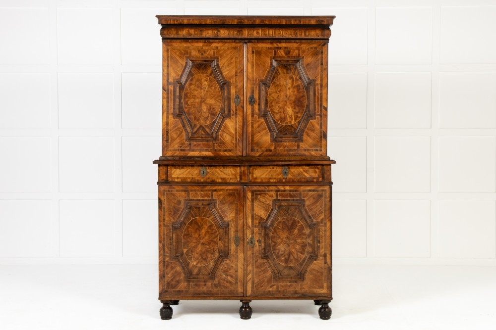 A two-tier seventeenth-century French walnut cabinet featuring geometric parquetry panels, central floral starburst inlays, two upper doors, two central drawers, two lower doors, and turned bun feet.