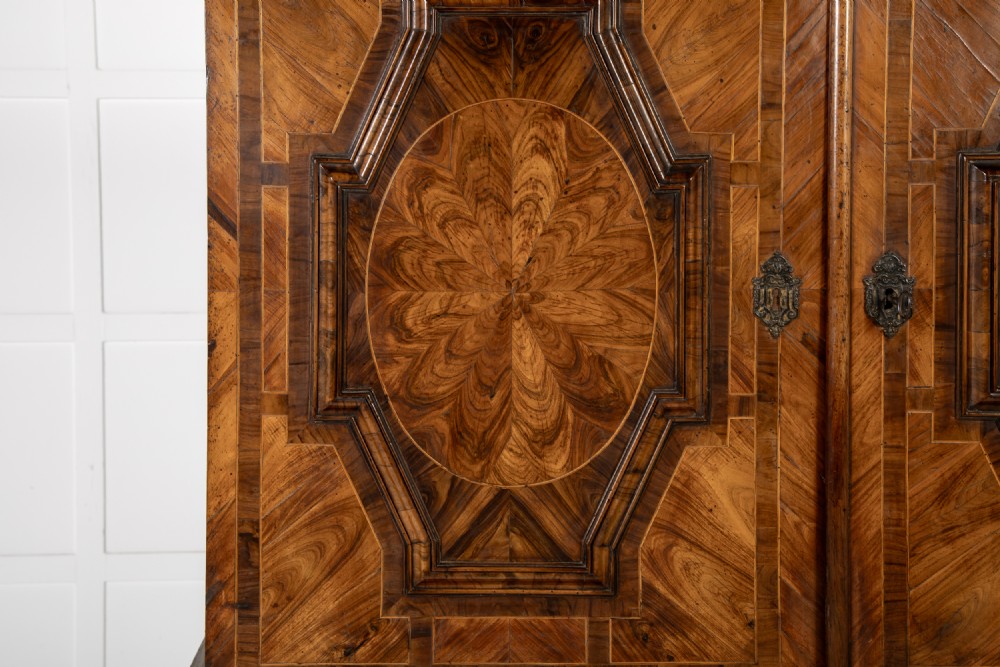 A two-tier seventeenth-century French walnut cabinet featuring geometric parquetry panels, central floral starburst inlays, two upper doors, two central drawers, two lower doors, and turned bun feet. View V