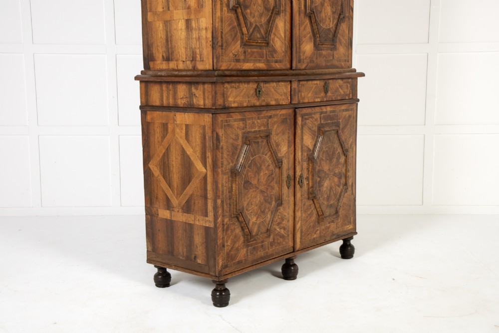 A two-tier seventeenth-century French walnut cabinet featuring geometric parquetry panels, central floral starburst inlays, two upper doors, two central drawers, two lower doors, and turned bun feet. View IX