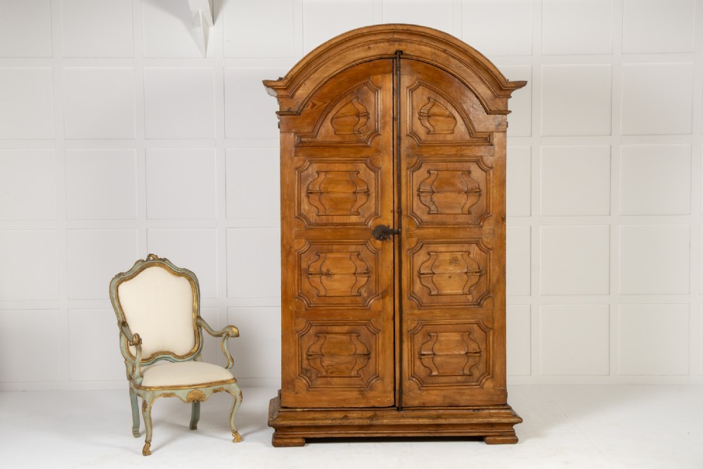 An eighteenth-century Italian pine armoire featuring an arched pediment, double doors with raised moulded panels, and wrought iron lock hardware.
