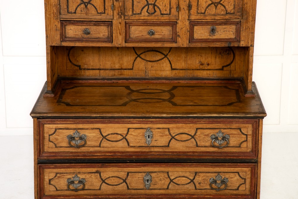An 18th-century two-part pine cabinet featuring an arched upper cupboard section decorated with black painted geometric scrollwork over a base with three wide drawers. View III