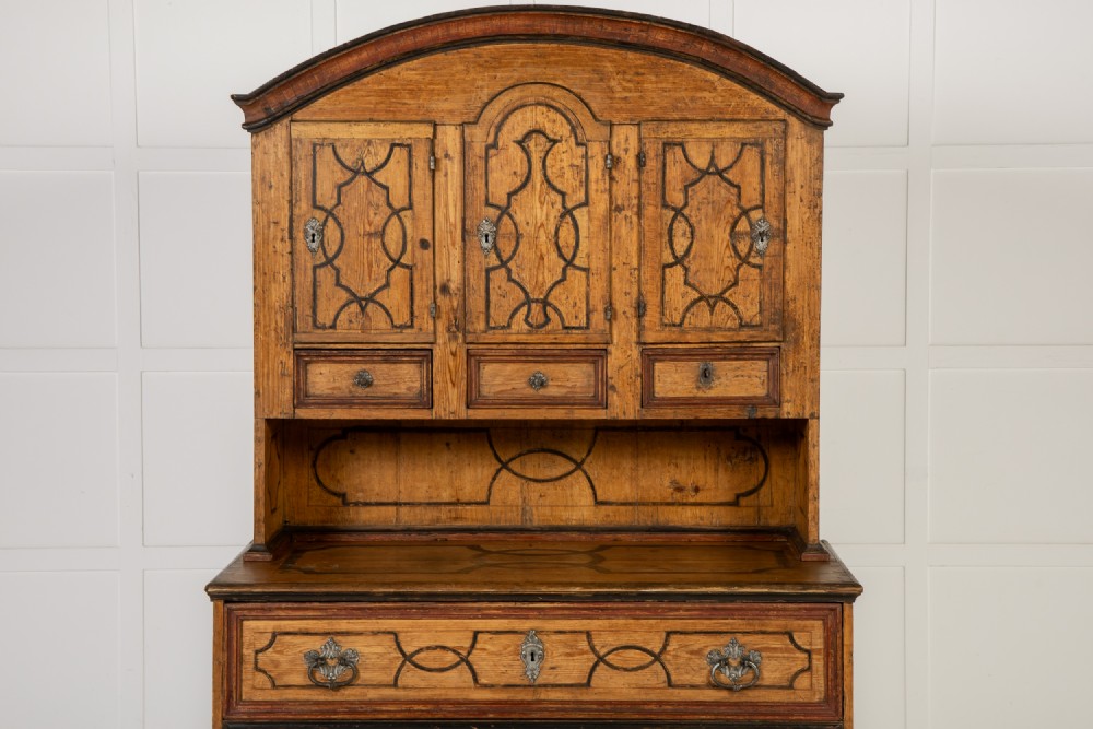 An 18th-century two-part pine cabinet featuring an arched upper cupboard section decorated with black painted geometric scrollwork over a base with three wide drawers. View IV