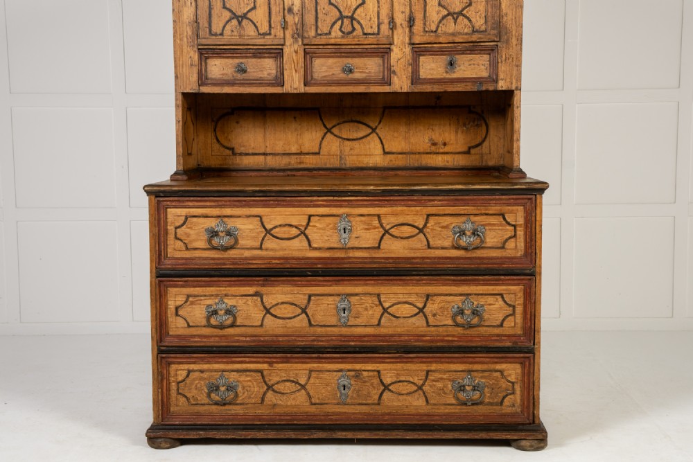 An 18th-century two-part pine cabinet featuring an arched upper cupboard section decorated with black painted geometric scrollwork over a base with three wide drawers. View V
