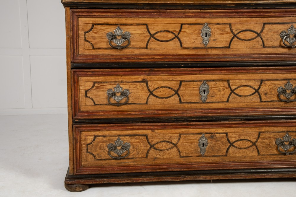 An 18th-century two-part pine cabinet featuring an arched upper cupboard section decorated with black painted geometric scrollwork over a base with three wide drawers. View VI