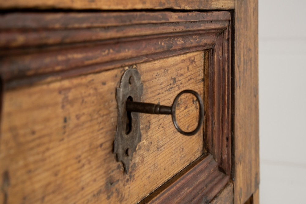 An 18th-century two-part pine cabinet featuring an arched upper cupboard section decorated with black painted geometric scrollwork over a base with three wide drawers. View X