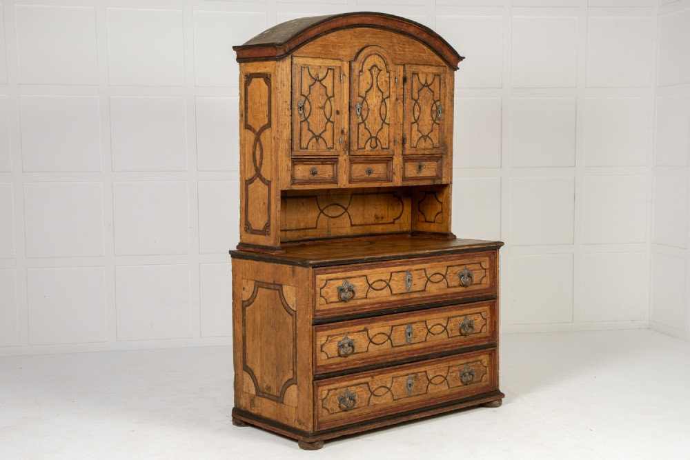 An 18th-century two-part pine cabinet featuring an arched upper cupboard section decorated with black painted geometric scrollwork over a base with three wide drawers. View XI