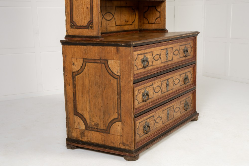 An 18th-century two-part pine cabinet featuring an arched upper cupboard section decorated with black painted geometric scrollwork over a base with three wide drawers. View XII